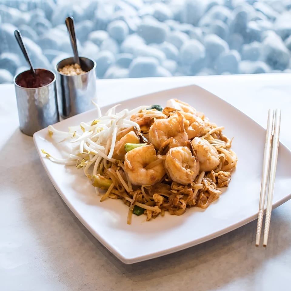 Shrimp Pad Thai with bean sprouts, lime, and chopsticks on a white plate.